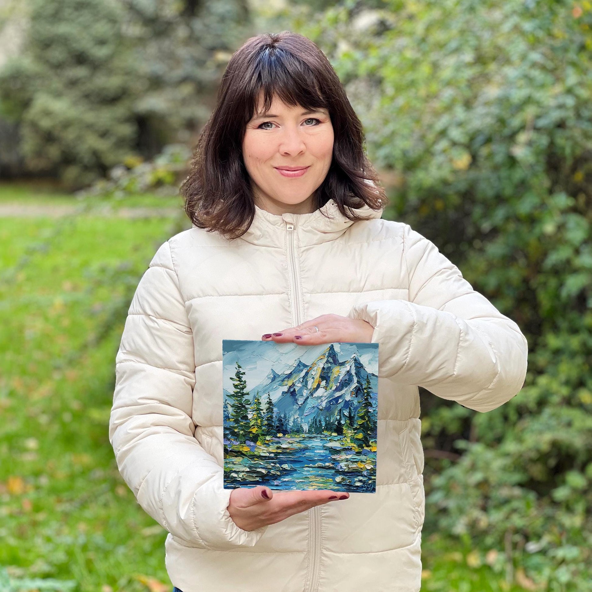 Hanna Hryharenka holding a painting of a mountain landscape outdoors