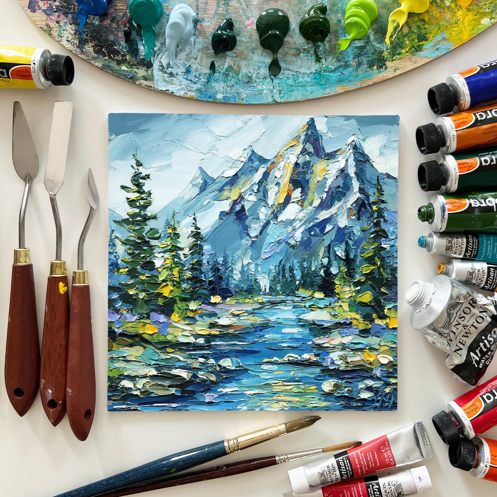Painting of a mountain landscape with art supplies on a white surface