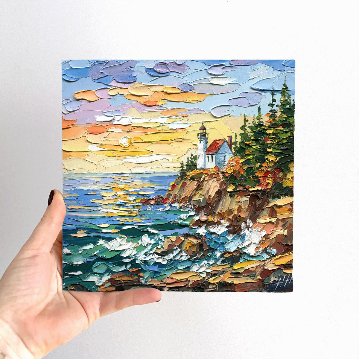 Unframed 8 × 8 inch Acadia Lighthouse oil painting held by hand, showing the square scale and front signature