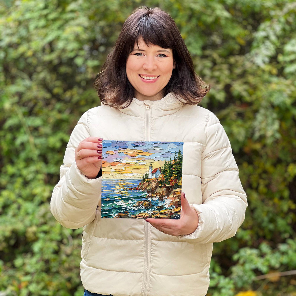 Hanna Hryharenka holding the 8 × 8 inch Acadia Lighthouse painting outdoors to show its scale